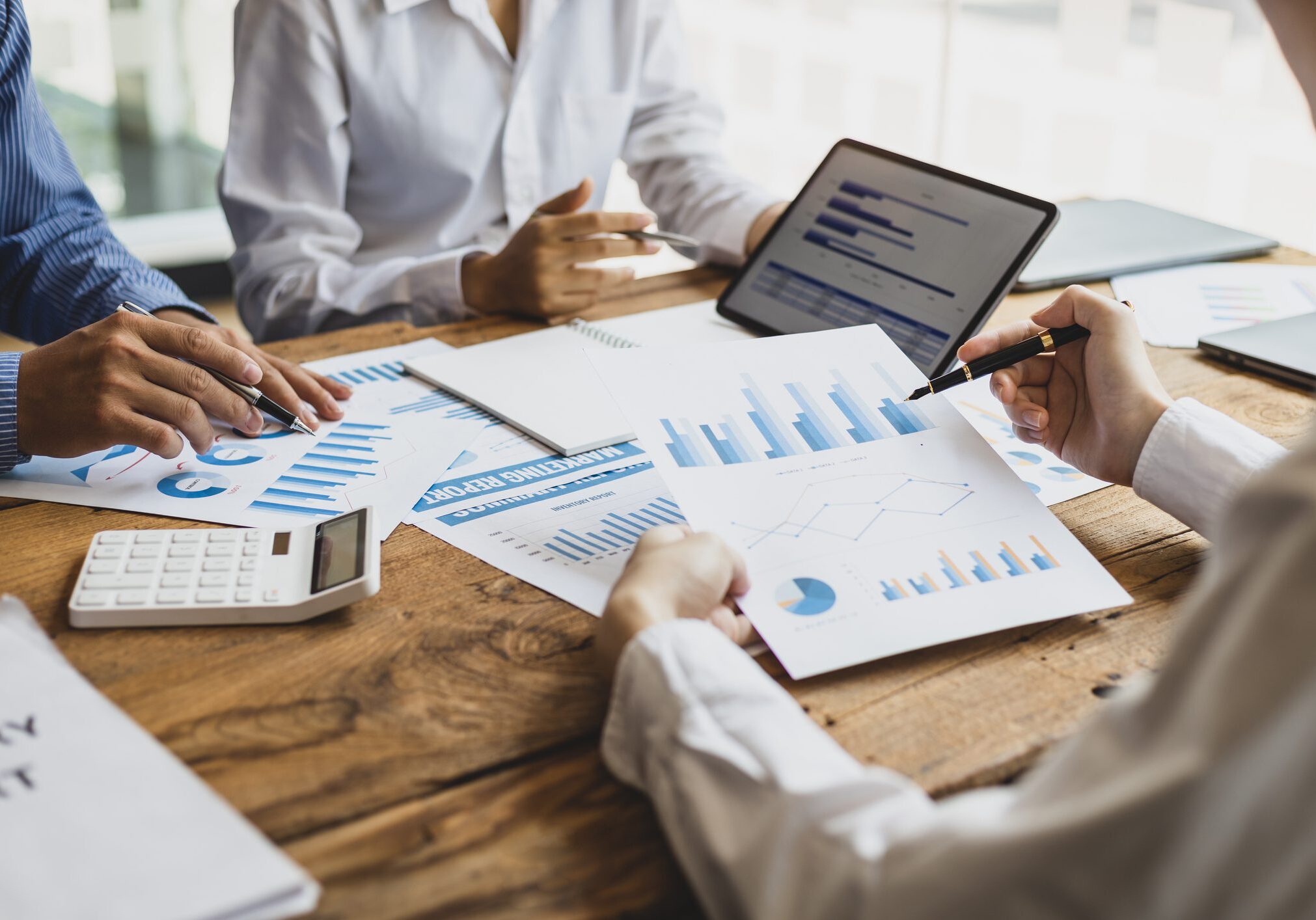 Business meeting, brainstorming sessions discuss analysis of investment growth graph and market charts in financial reports and business investment strategy planning. Blessed Team Consulting LLC